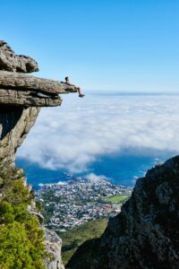 Traveller sitting on cliff at Table Mountain overlooking Cape Town coastline in South Africa