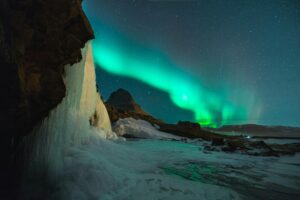 Northern Lights glowing over rugged Iceland coastline during winter adventure travel.
